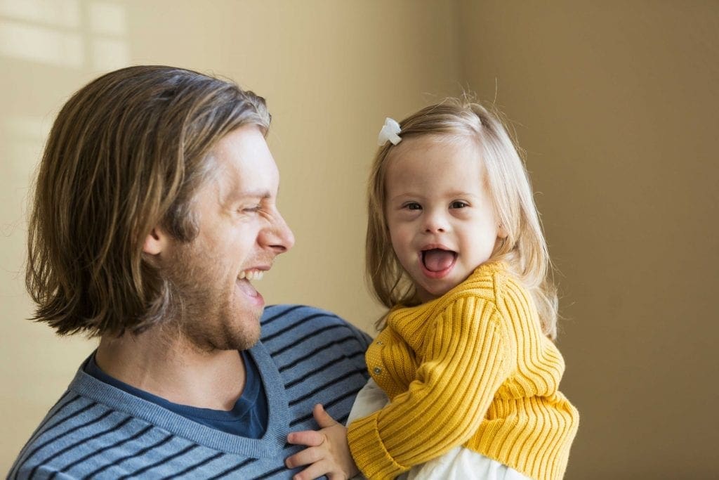 father smiling holding young daughter with down syndrome