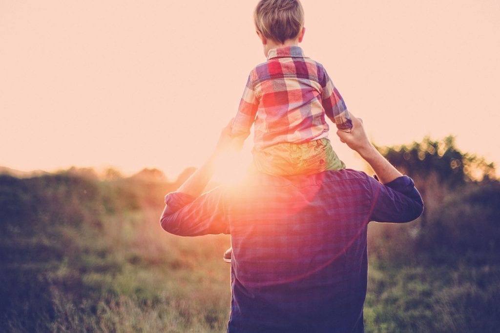 A man with toddler on shoulders outdoors with sunlight