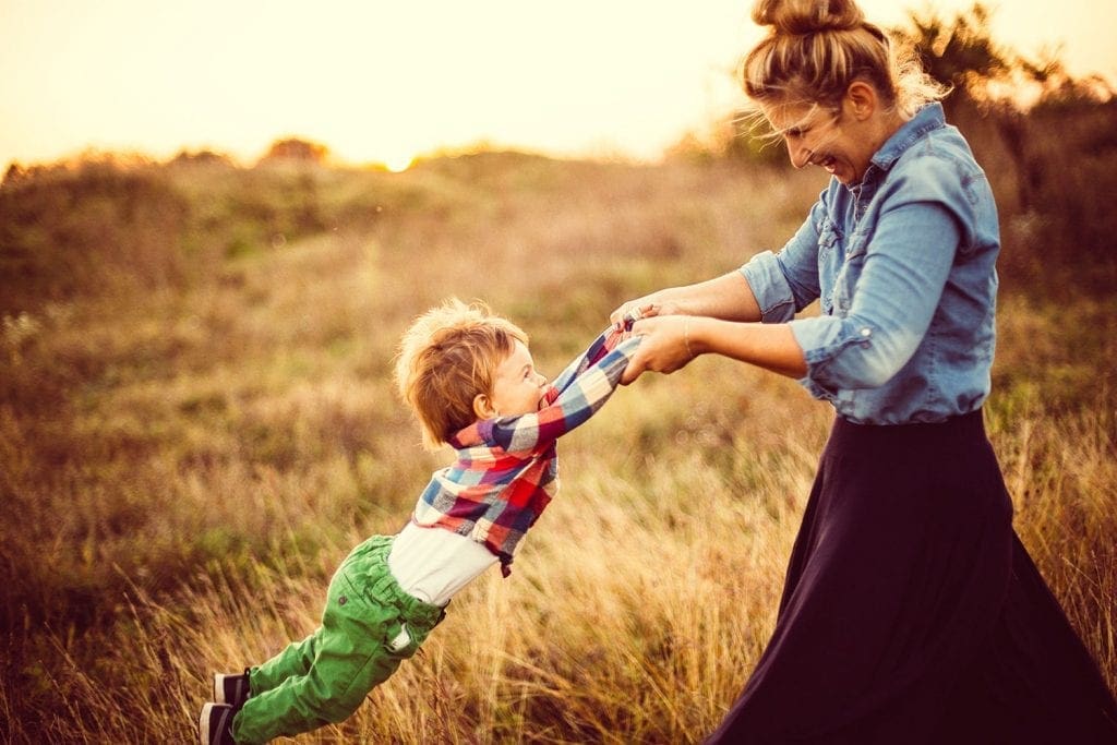 A happy mother in a field spinning around her happy young son