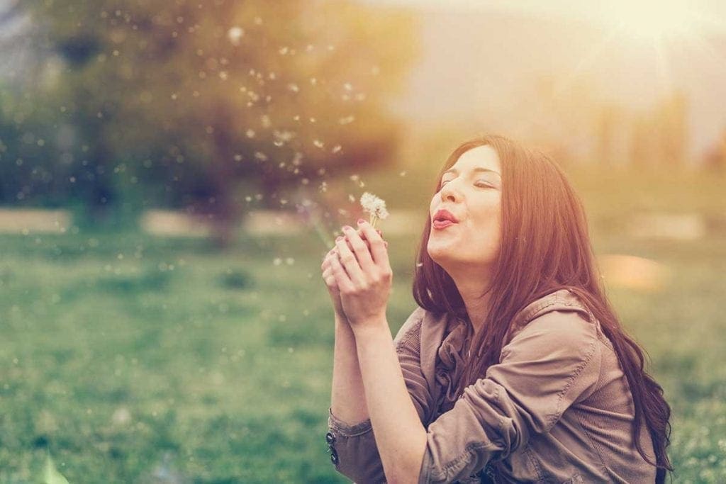 lady blowing dandelion sitting on grass