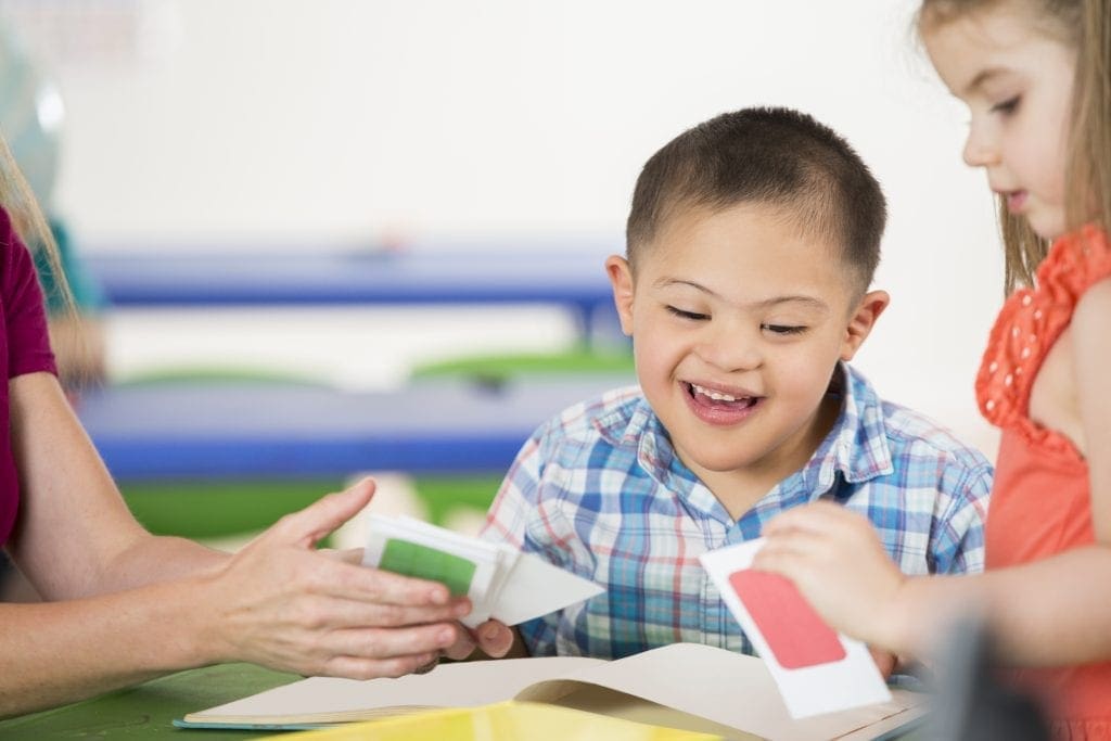 Cute Hispanic preschool age boy with Down's Syndrom smiles while playing with flash cards with his therapist and a female student.
